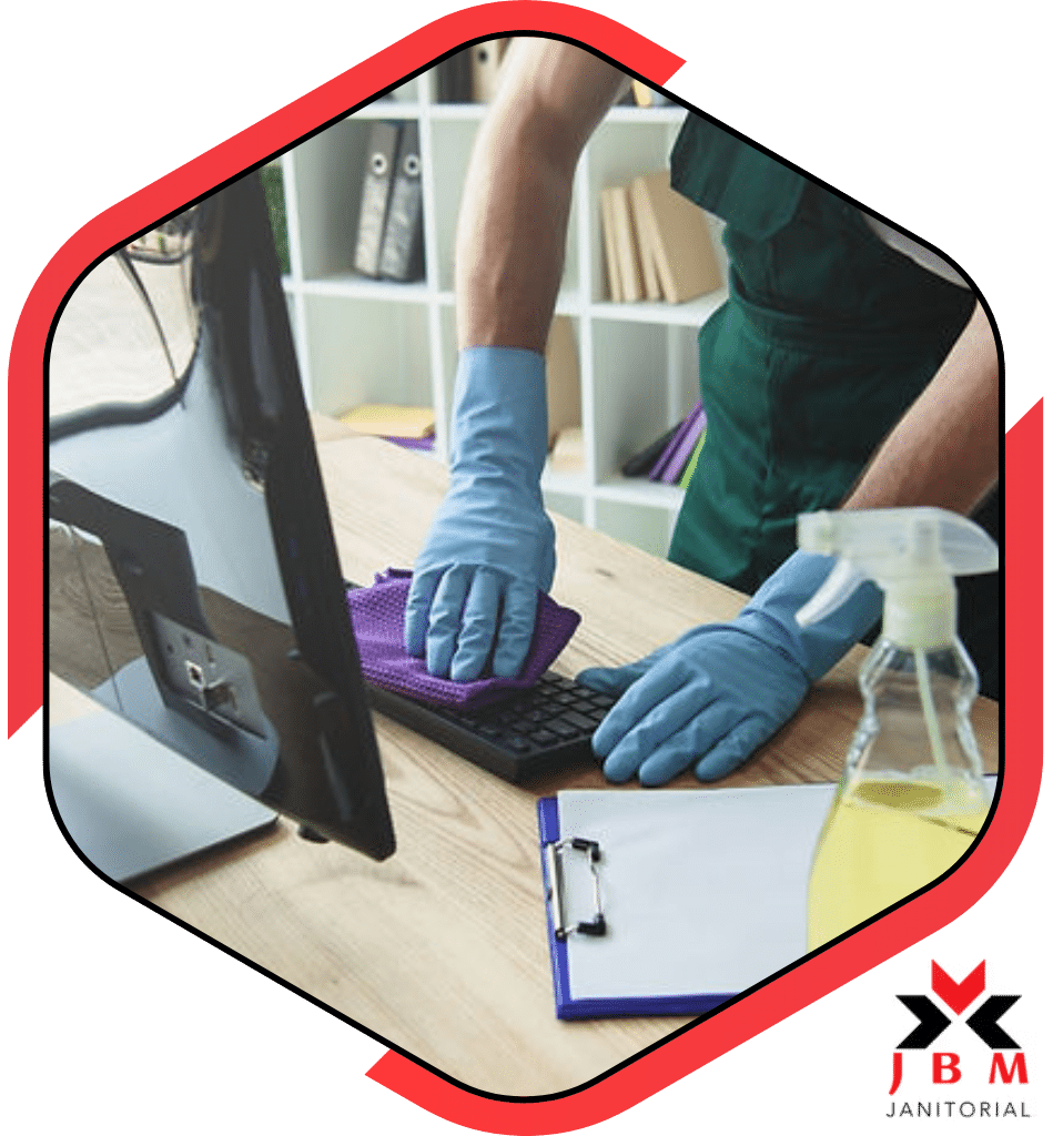 Janitorial cleaning professional wiping down office desk and keyboard with cleaning supplies, offering office cleaning services for businesses seeking a clean and sanitized workspace.