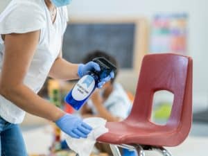 Cleaning a chair with disinfectant spray to maintain school hygiene and prevent the spread of germs.