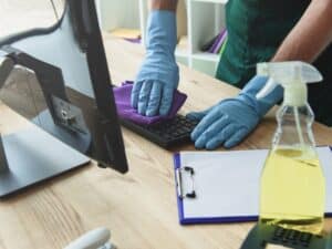 Close-up of hands applying safe cleaning techniques to sanitize a keyboard using a microfiber cloth and cleaning solution.