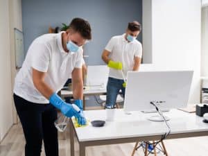 Two people cleaning an office to prevent dust build-up and maintain a tidy workspace.