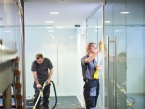 Professional cleaners highlighting the importance of dusting glass surfaces in an office for a clean environment.