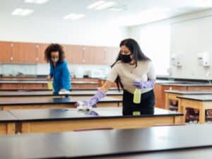 Two people cleaning a classroom to reduce bacteria from school bathrooms and maintain a hygienic environment.