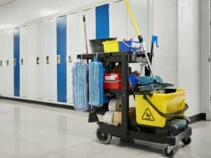 Cleaning supplies cart in hallway promoting a clean school environment with mops, buckets, and paper towels.